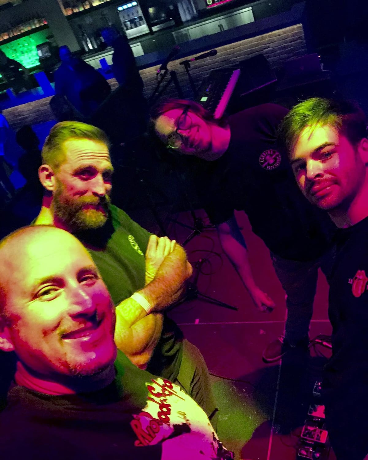 Four Los Rios Rock School instructors crowded into a phone photo backstage under magenta and green stage lighting